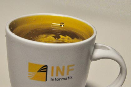 Ein Wassertropfen fällt in eine Tasse mit dem "Fakultät Informatik" - Logo.