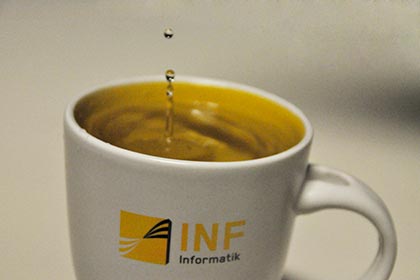 Ein Wassertropfen fällt in eine Tasse mit dem "Fakultät Informatik" - Logo.